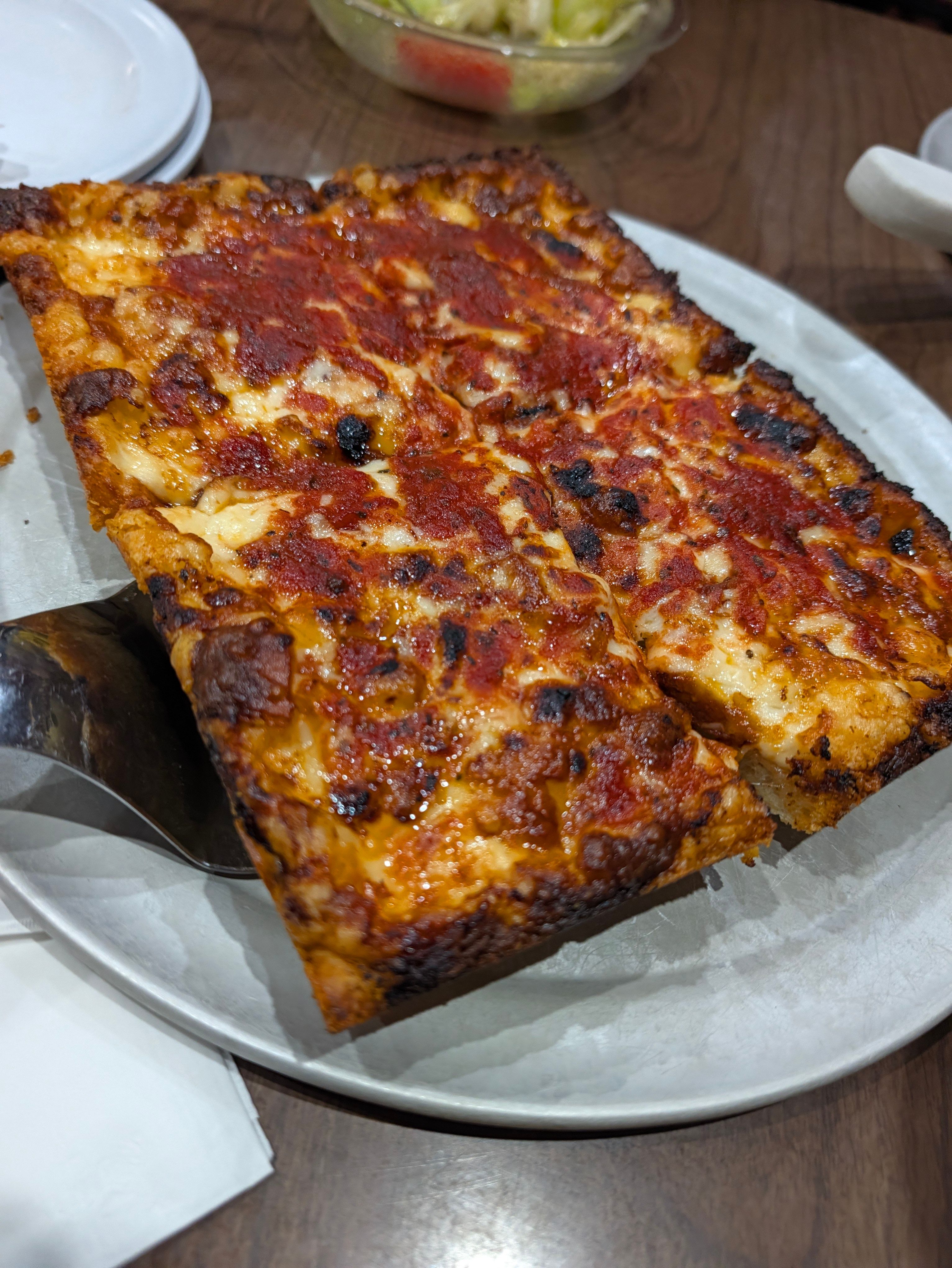 Two squares of Detroit-style pizza on a metal spatula, red sauce on top and a charred cheese edge