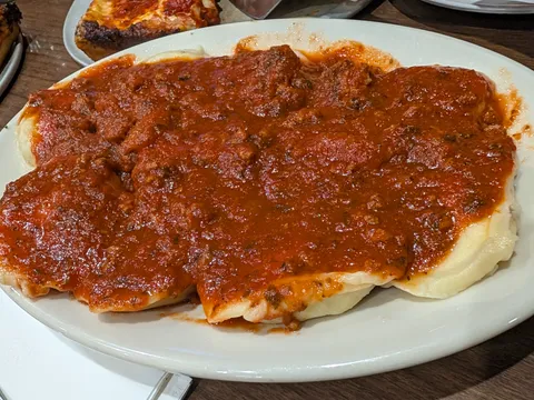 Meat ravioli covered in meat sauce on a white oval plate