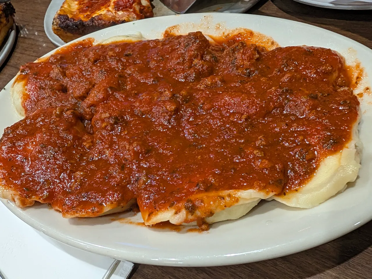 Meat ravioli covered in meat sauce on a white oval plate