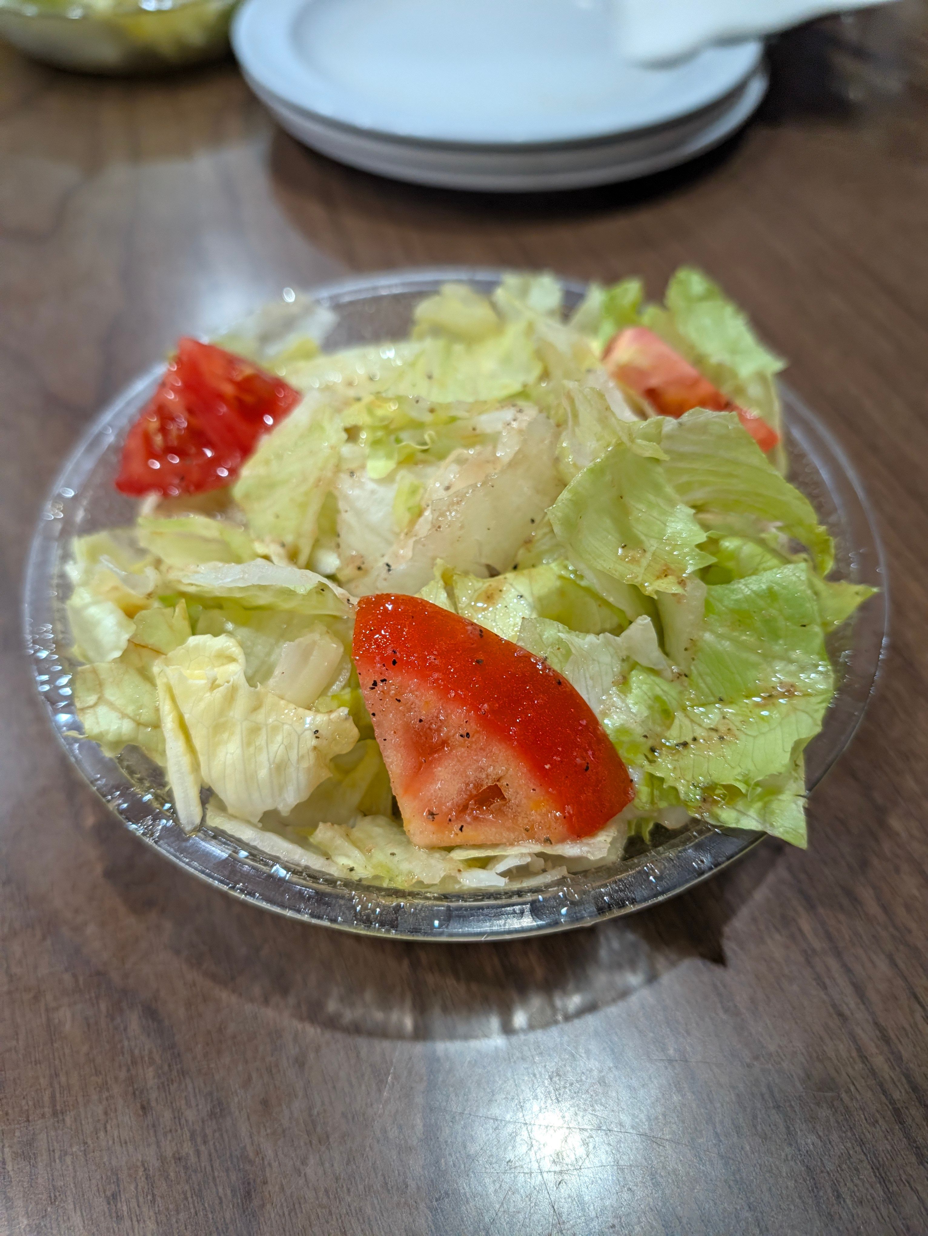 Iceberg lettuce and tomato wedges with vinaigrette and black pepper in a glass bowl